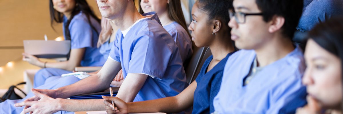 A multi-ethnic group of students sit in the university lecture hall. One student holds his smart phone.